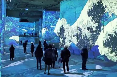An exhibit with large ocean waves and blue hues, and attendees in silhouette.